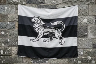 Drapeau breton Gwenn-ha-Du accroché sur le mur en granit d'une chapelle médiévale bretonne, symboles hermine visibles en gros plan
