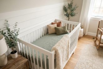 Lit de bébé en bois blanc avec parure en lin vert sauge et couverture tricotée dans un coin de chambre naturelle et apaisante