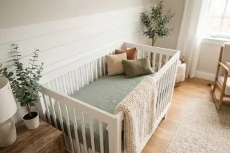 Lit de bébé en bois blanc avec parure en lin vert sauge et couverture tricotée dans un coin de chambre naturelle et apaisante